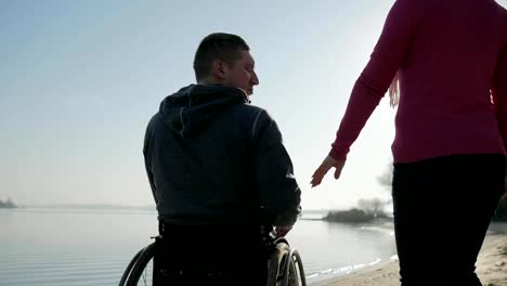 Man-in-wheelchair-takes-girlfriends-hand-and-look-out-onto-the-river