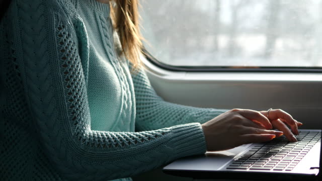 Weibliche-Hände-Tippen-auf-Tastatur-von-Laptop-im-Zug.-Frau-während-der-Eisenbahn-unterwegs-mit-Freunden-chatten.-Junges-Mädchen-mit-Notebook.-Arm-drucken-Sie-eine-Nachricht.-Nahaufnahme