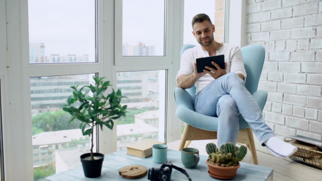 Hombre-atractivo-con-tableta-digital-sentado-en-silla-en-el-balcón-en-Apartamento-moderno-tipo-loft