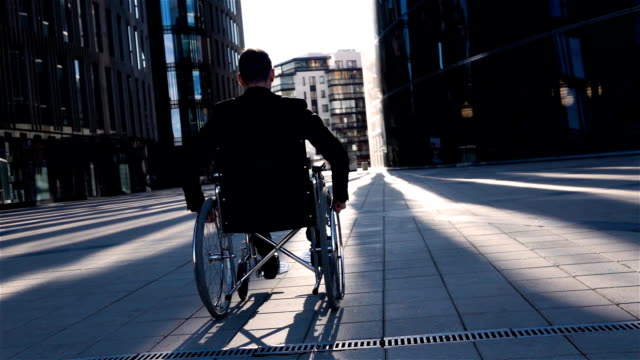 Back-view-of-a-disabled-businessman-in-wheelchair,-moves-in-business-district