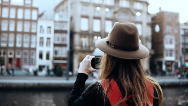 Tourist-lady-takes-photos-of-old-architecture.-Girl-with-long-hair-and-red-backpack-enjoying-amazing-city-scenery.-4K