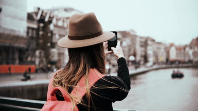 Young-girl-takes-photos-and-talks-on-the-phone.-Beatiful-woman-journalist-with-long-hair-and-red-backpack-working.-4K