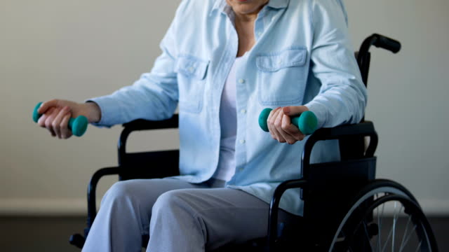 Reife-Dame-im-Rollstuhl-sitzen-und-versuchen,-heben-Sie-Hanteln,-rehabilitation