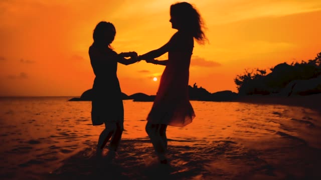 zwei-glückliche-tanzende-Mädchen-Hand-in-Hand-am-Strand-bei-Sonnenuntergang-in-Zeitlupe