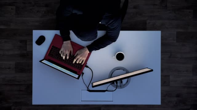 Junger-Mann-in-schwarzer-Hoodie-hinter-Schreibtisch-sitzt,-auf-Laptop-eingeben-und-dann-weglaufen,-wenn-Lichter-während-Top-Nachtaufnahme-einschalten