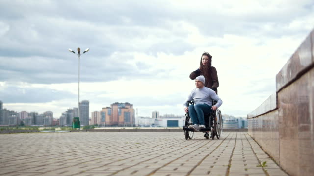 Hombre-discapacitado-en-silla-de-ruedas-con-mujer-joven-caminando-en-la-calle-de-la-ciudad