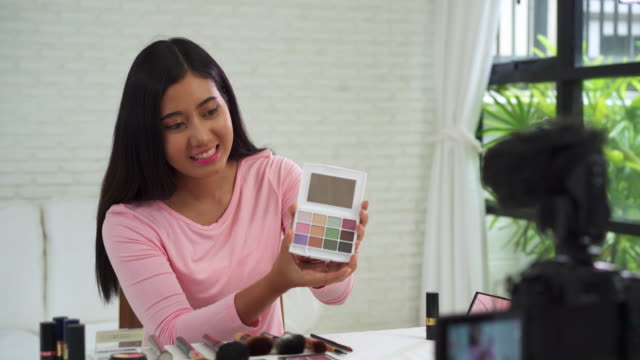 Beauty-blogger-present-beauty-cosmetics-while-sitting-in-front-camera-for-recording-video.-Beautiful-woman-use-brush-while-review-make-up-tutorial-broadcast-live-video-to-social-network-by-internet.