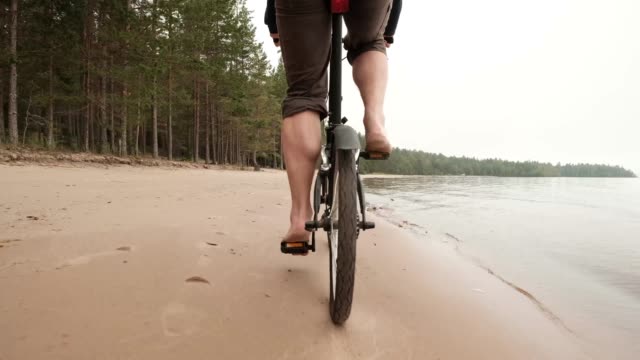 A-barefooted-man-riding-a-bicycle-on-the-beach.-Relaxing-while-having-a-vacation-by-the-lake.