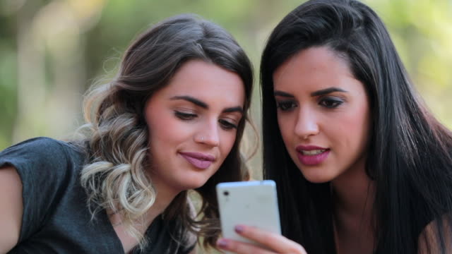 Girlfriends-looking-at-their-cellphones-sharing-social-media-gossip-outdoors