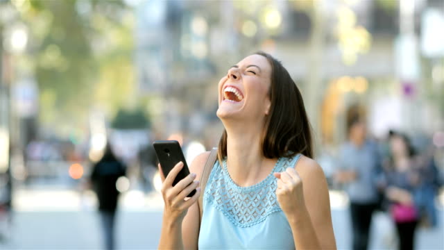 Mujer-emocionada-leyendo-noticias-en-un-teléfono-en-la-calle