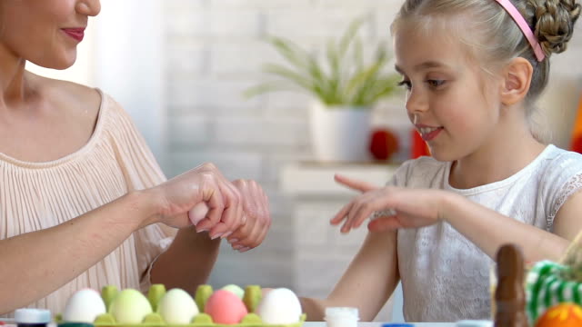 Hija-elegir-huevo-rosa-en-manos-de-las-madres,-familia-jugando-en-los-juegos-de-Pascua