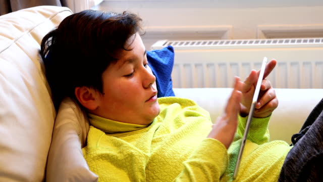 Kind-liegt-auf-einem-Sofa-mit-digitalem-Tablet-Computer