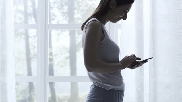Woman-walking-in-the-bedroom-and-chatting-with-her-phone