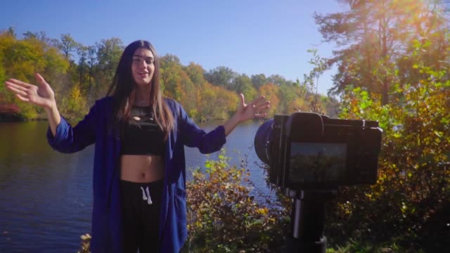 Blogging-young-woman-stand-next-to-camera-at-nature-talking-and-gesturing-and-smiling-slow-motion