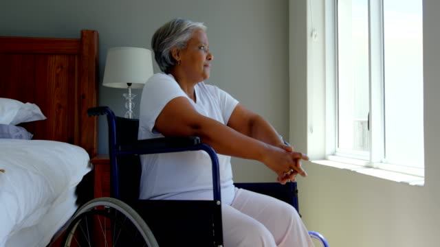 Seitenansicht-der-Behinderung-senior-schwarze-Frau-sitzen-im-Rollstuhl-in-der-Nähe-von-Fenster-im-Schlafzimmer-zu-Hause-4k