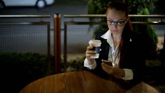 beautiful-young-Caucasian-woman-sitting-after-work-in-the-evening-in-a-street-cafe-drinking-coffee-and-chatting-on-social-networks-using-a-smartphone.