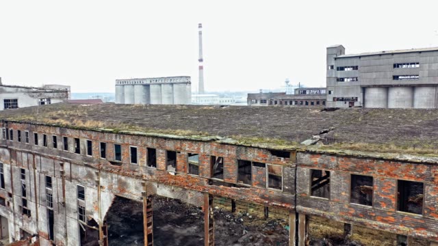 Ein-alter-verlassener-Fabrikhangar-mit-beschädigten-Wänden-auf-dem-Hintergrund-anderer-alter-Bauwerke-im-gleichen-Bereich.