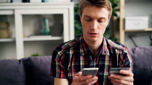 El-hombre-joven-está-haciendo-el-pago-en-línea-con-tarjeta-bancaria-usando-el-teléfono-inteligente-en-casa