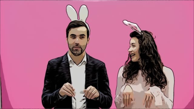 Young-beautiful,-tender-creative-pair-standing-on-a-pink-background.-At-the-same-time,-fooling-shows-the-movements-of-bunnies.-Dressed-in-a-hook-ears.-Easter.-Motions.