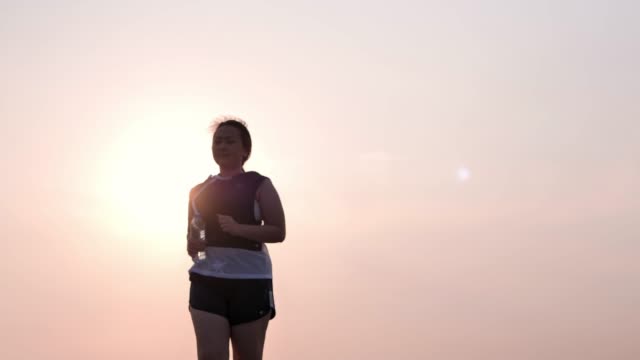 Übergewichtige-asiatische-Frauen-joggen-am-frühen-Morgen-im-Sonnenlicht-auf-der-Straße.-Konzept-des-Gewichtsverlustes-mit-Bewegung-für-die-Gesundheit.