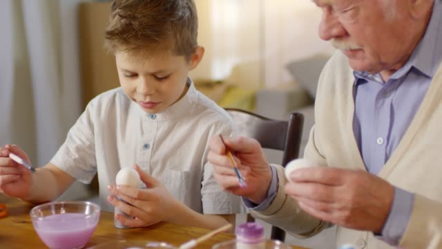 Abuelo-enseñando-nieto-a-pintar-huevos