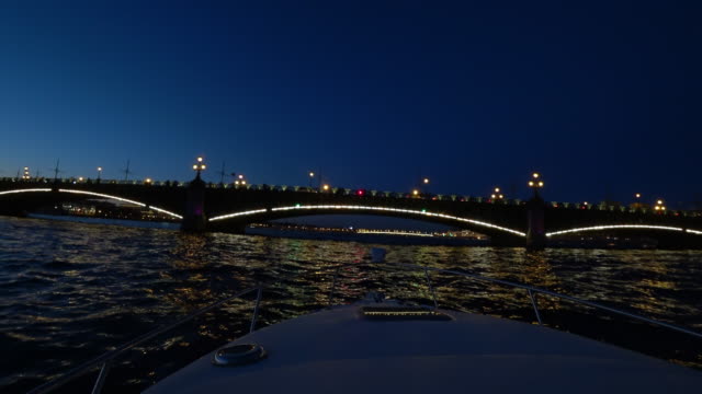 Center-of-St.-Petersburg,-Russia-at-night.-On-the-river-pass-passenger-boats.-The-ship-turns-on-the-water-and-floats-towards-the-bridge