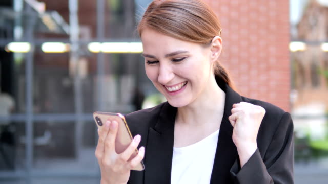 Outdoor-Young-Businesswoman-Excited-for-Success-on-Smartphone