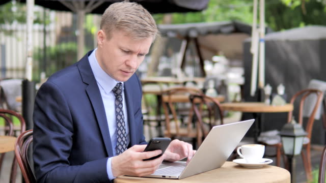Geschäftsmann-nutzt-Smartphone-und-Laptop-im-Outdoor-Cafe