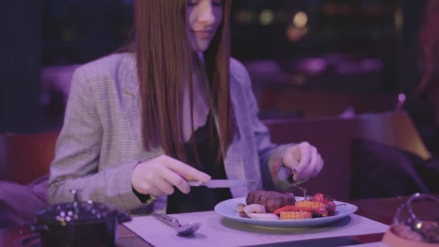 Nette-junge-Frau-essen-Fleisch-mit-Gemüse-im-modernen-Restaurant-gegrillt.