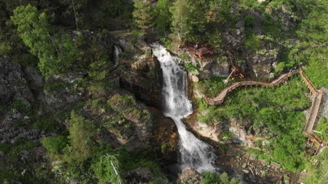 Drone-sobrevolando-un-bosque-verde-con-cascada-en-las-montañas-altai