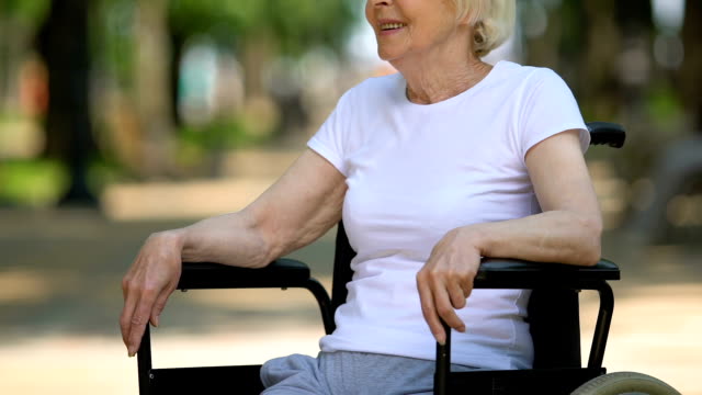 Mature-woman-sitting-in-wheelchair-on-hospital-territory,-rehabilitation