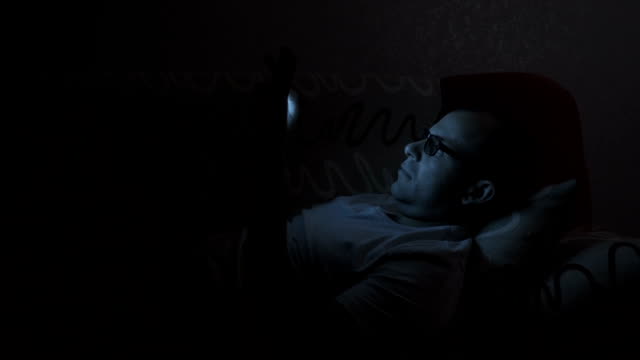 Close-up-of-man-with-glasses-using-smartphone.-Young-man-with-tablet-computer.-A-man-at-night-on-social-networks-using-a-smartphone.-Man-with-tablet-computer-lying-on-sofa