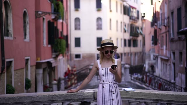 Slow-motion-effect-of-young-beautiful-female-tourist-recreating-on-italian-bridge-near-canal-in-Venice