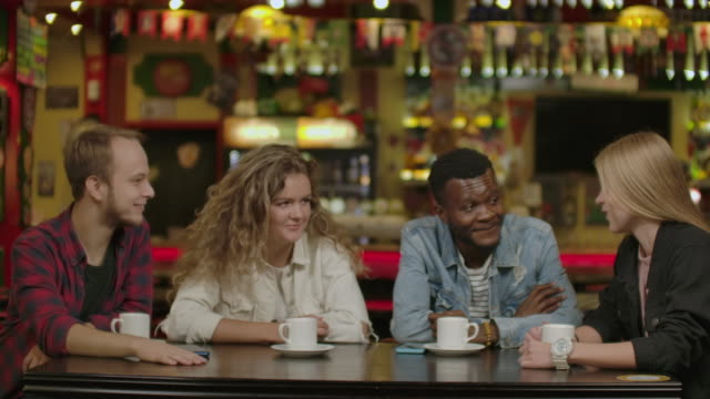 Happy-multiracial-young-people-friends-talking-laughing-at-group-meeting-sharing-cafe-table,-diverse-students-drinking-coffee-having-fun-together-enjoy-multi-ethnic-friendship-pleasant-conversation.