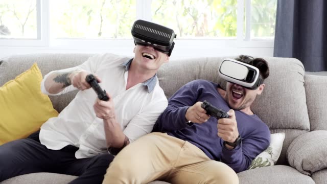 Gay-couple-relaxing-on-couch-playing-virtual-reality-games.-Exciting-mood.-Turning-hard.
