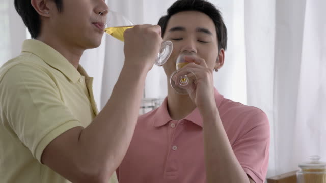 Pareja-asiática-gay-celebrando-en-casa.-Niño-gay-bebiendo-bebida-para-la-emoción-feliz-aniversario-de-amor-juntos.-Concepto-de-estilo-de-vida,-familia,-gay-y-bisexual.