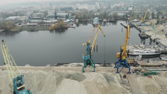 Aerial-view-of-industrial-city-and-cargo-working-cranes-in-docks-extracting-river-sand-from-iron-barge