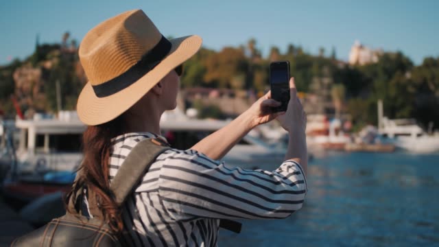 Millennial-hipster-mujer-turista-en-traje-casual-con-mochila-fotografiando-en-marina