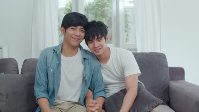 Porträt-Junge-asiatische-Homosexuell-Paar-gefühl-glücklich-lächeln-zu-Hause.-Asiatische-LGBTQ-Männer-entspannen-zu-schüchtern-Lächeln-blickend,-während-auf-dem-Sofa-im-Wohnzimmer-zu-Hause-im-Morgen-Konzept-liegen.