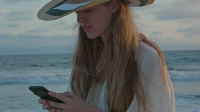 Young-woman-at-the-beach-texting-by-the-ocean-during-sunset