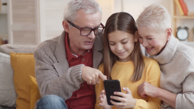 Neugierige-kaukasische-Großeltern-beobachten-Enkelin-mit-Smartphone