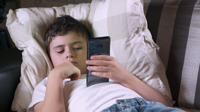 Teenager-Junge-liegt-auf-einem-Sofa-und-spielt-ein-Spiel-auf-seinem-Smartphone.-Social-Media-und-Kind.-Handy--und-Gerätetechnik.-Telefon-und-Kindheit.-Kind-und-Telefon-im-Leben.-Zelle-und-Gadget.