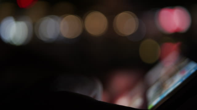 Person-using-digital-tablet-device-at-night-with-city-lights-in-background---out-of-focus-blurry-concept-footage