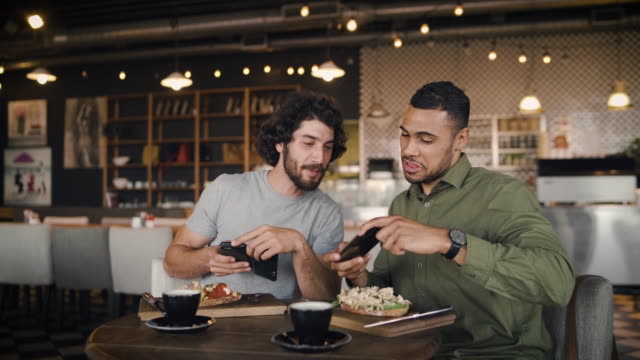 Junge-afroamerikanische-Mann-mit-kaukasischen-Freund-klicken-Foto-mit-Smartphone-der-italienischen-Bruschetta-mit-Kaffee-im-Café-beim-Mittagessen-im-modernen-Café
