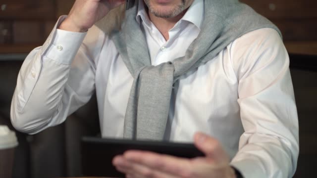Mann-in-Brillen-Reifen-befasst-sich-mit-der-Tablette-und-spricht-auf-dem-Handy-im-Internet-café