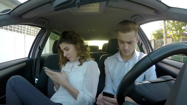 Two-teenagers-using-social-media-on-their-smart-phones-while-sitting-in-the-car