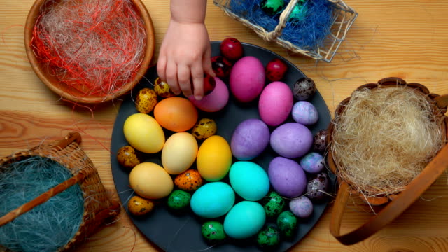 Child's-hand-takes-and-lays-colored-easter-eggs-in-different-baskets