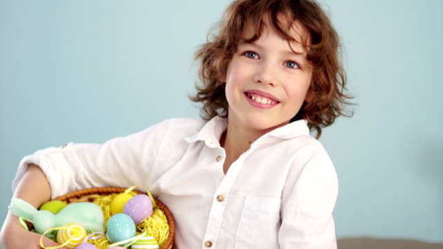 Curly-red-haired-child-in-a-white-shirt-with-a-figure-of-an-Easter-bunny-and-a-set-of-Easter-eggs-in-a-basket.-A-boy-laughs-cheerfully.-Slow-Motion.