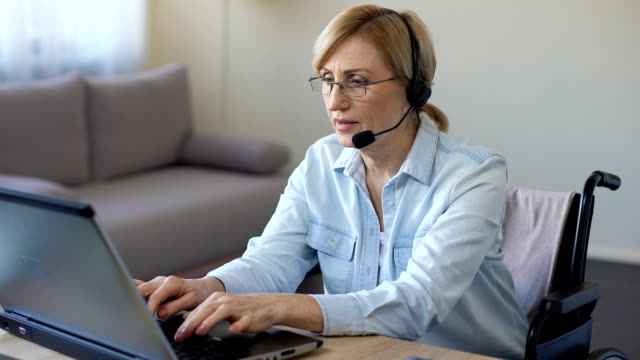 Call-center-female-operator-working-with-client-typing-on-laptop,-disabled-woman