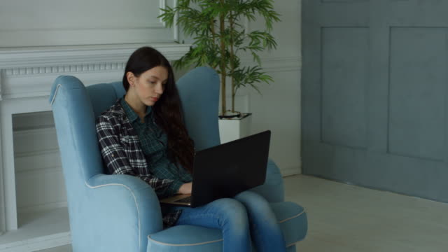 Elegant-woman-in-armchair-chatting-online-via-laptop